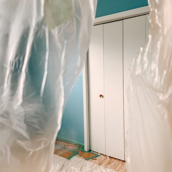 Plastic hangs from the door opening to the bedroom, with the blue paint and white closet doors showing through an opening.