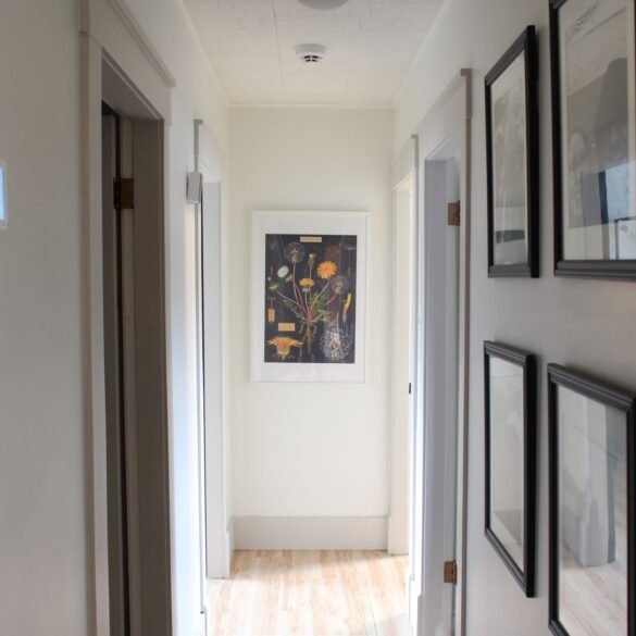 A hallway with 4 doors, 2 on either side. Walls are painted white and trim is beige. On the right side of the hallway, there are 2 rows of pictures with 3 in row. The frames are black with black and white photos.