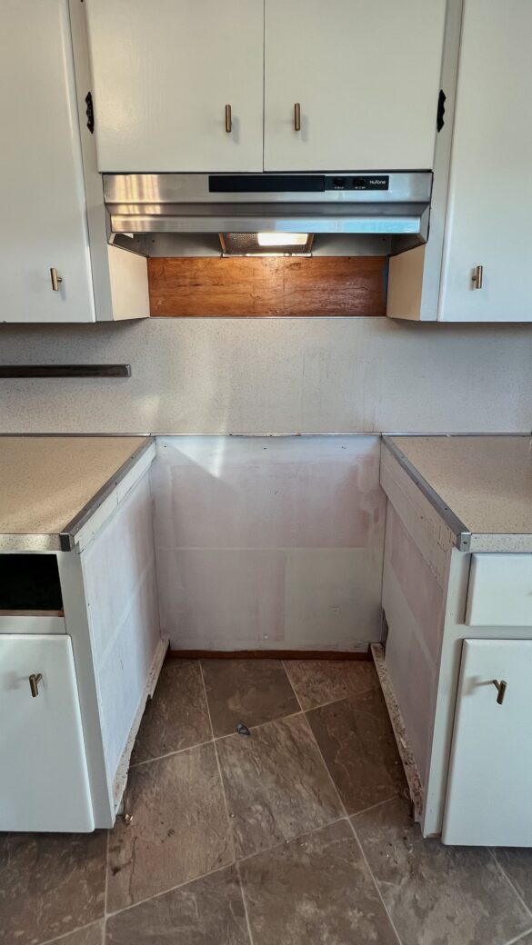 phase 3 kitchen renovation. a close up of the spoke where the range once sat, ad the hood vent. you can see the plywood behind the melamine backsplash, and primed plywood cabinets.