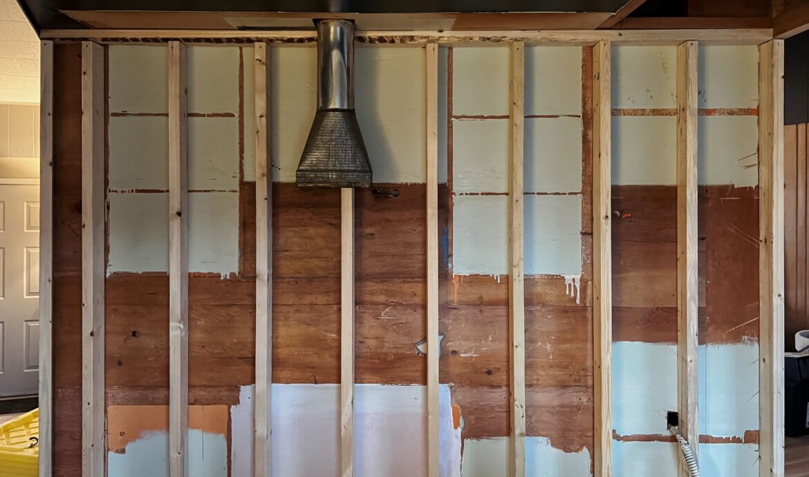 The wall is framed, with all cabinets removed. You can see the plywood behind the framing, with painted squares showing where the cabinets used to live. 