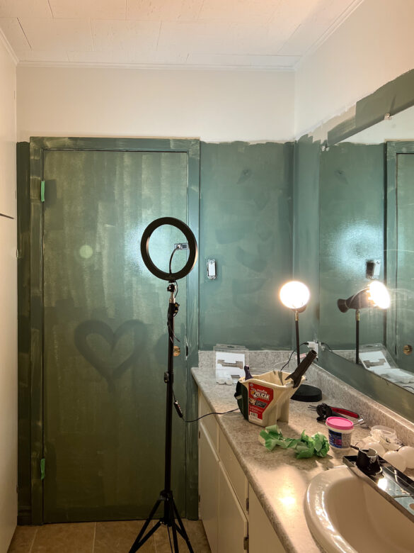 progress photo of a washroom being painted green. the paint is thin but you can see a heart is darker where a second coat started to be applied