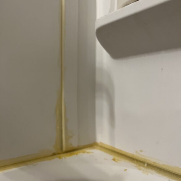 close up of corner in a shower surround with caulk that has gone yellow